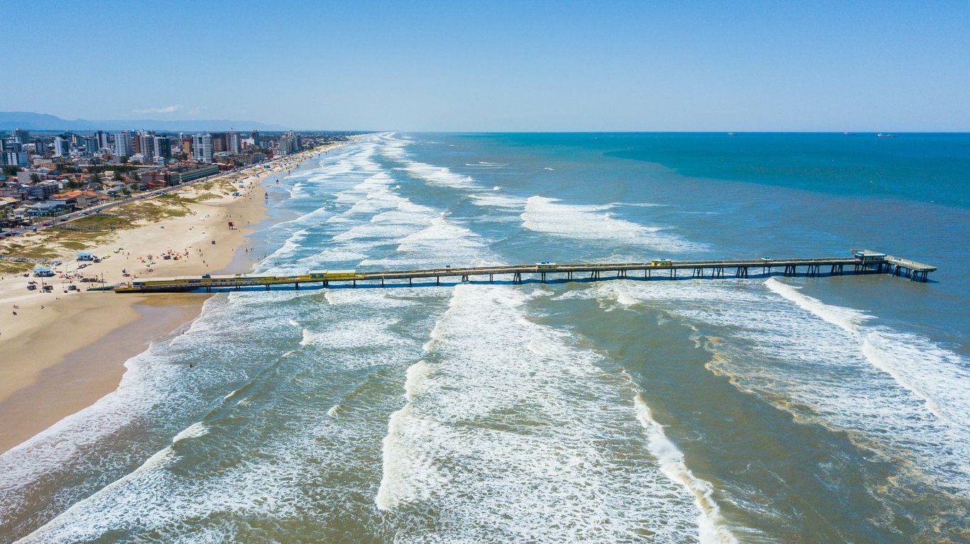Praia urbana no Litoral Norte do RS, com píer sobre as ondas
