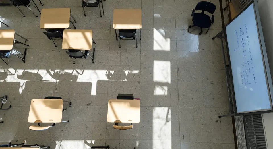 Sala de aula universitária vazia com mesas, cadeiras e quadro, iluminada por luz natural