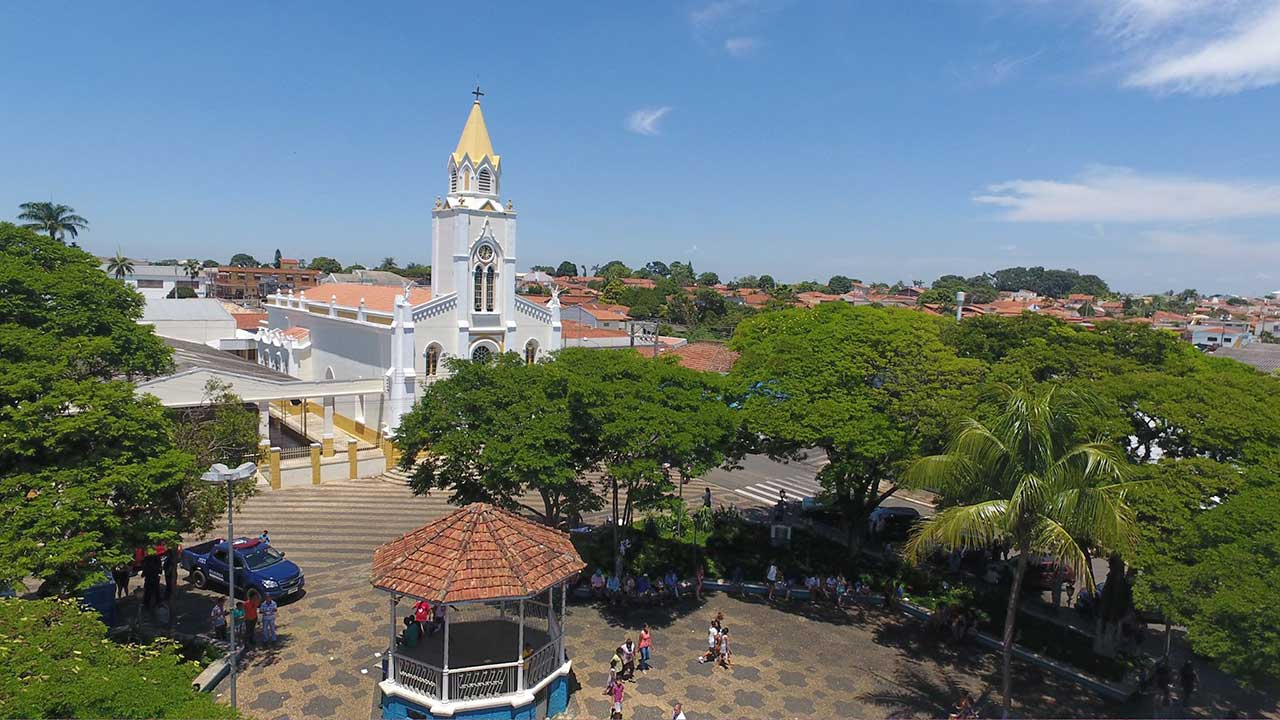 Praça central no interior de São Paulo, com igreja ao fundo e morros na paisagem