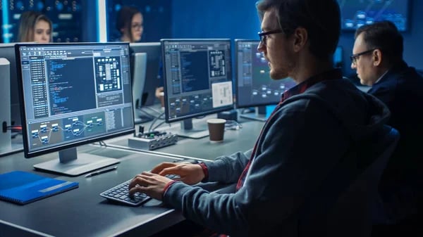 Equipe de tecnologia trabalhando em escritório moderno, com múltiplos monitores e colaboração em tempo real