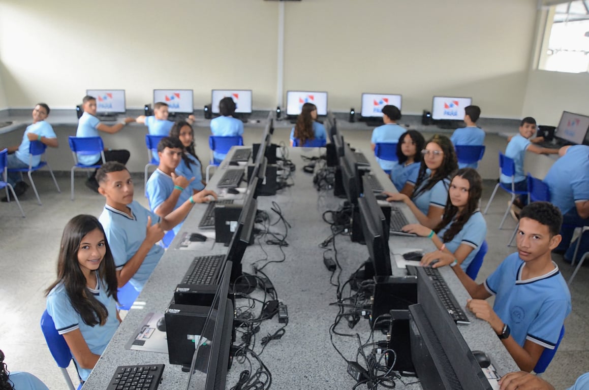 Sala de aula moderna com estudantes em uniforme utilizando computadores durante uma aula, ambiente iluminado e organizado