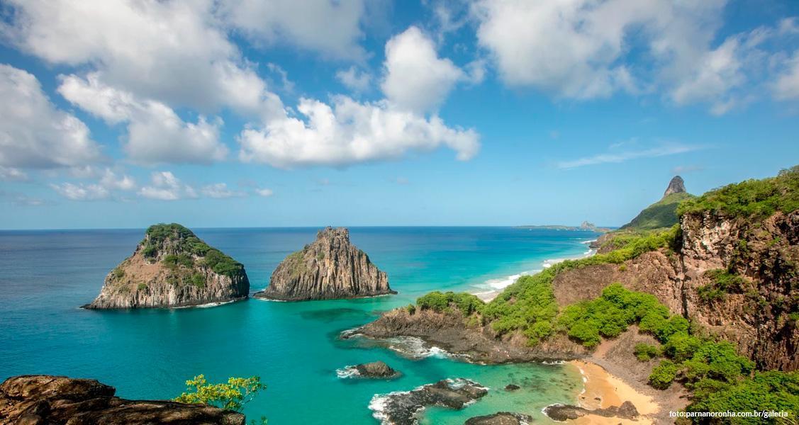 Vista aérea de Fernando de Noronha, com ilhas e mar azul-turquesa sob céu parcialmente nublado