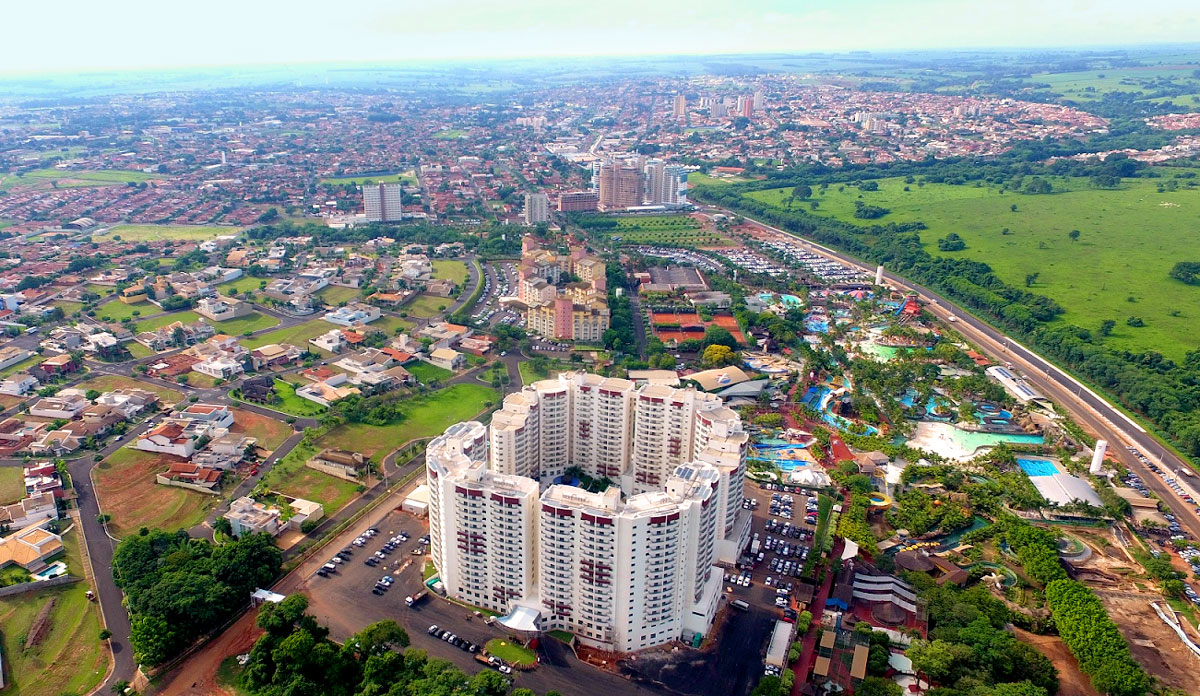 Vista aérea de Olímpia SP ao entardecer, com áreas urbanas e vegetação ao fundo
