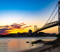 Vista de Florianópolis ao entardecer com a Ponte Hercílio Luz iluminada.