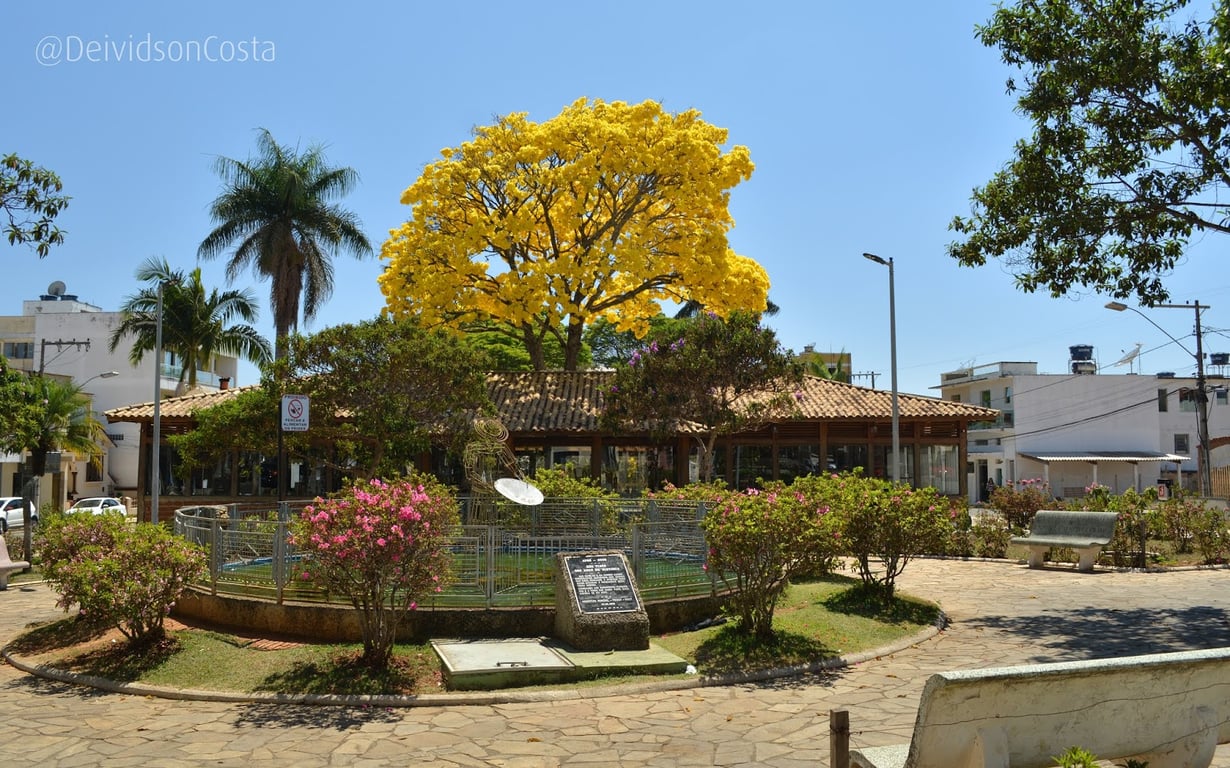 Praça central de São Tiago (MG) com ipê amarelo em destaque.