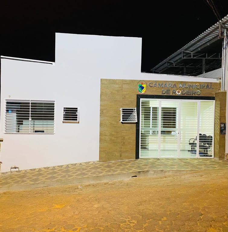 Fachada da Câmara Municipal de Rodeiro à noite, com bandeira e jardins frontais