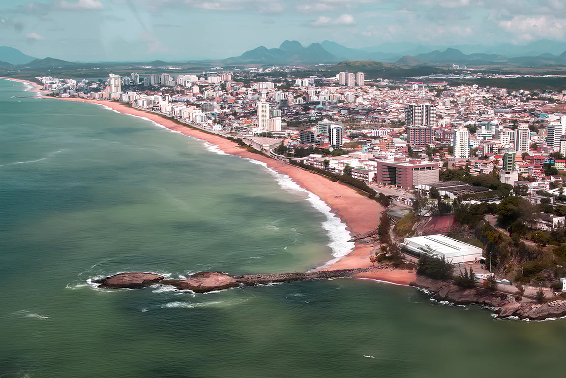 Vista aérea da costa urbana do Norte Fluminense, com praia e edifícios em composição horizontal