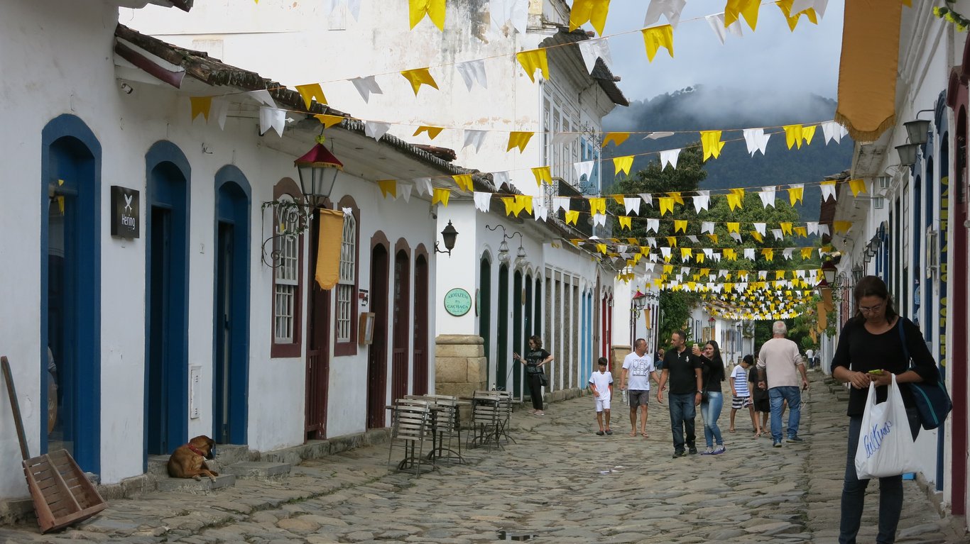 Cena urbana em pequena cidade do Nordeste, com casas coloridas e pessoas caminhando em dia ensolarado