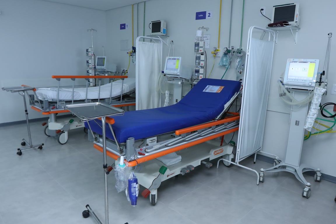 Profissionais de saúde atendendo em uma unidade básica, com equipamentos clínicos ao fundo