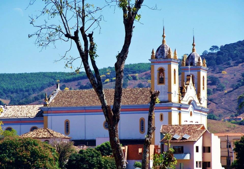 Cidade do interior de Minas Gerais com morros ao fundo, em composição horizontal, representando o cenário típico da Zona da Mata