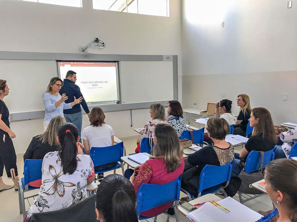 Sala de aula moderna, com estudantes e lousa digital, ambiente que remete ao ensino público tecnológico