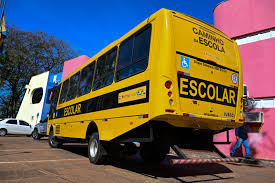 Ônibus escolar amarelo em via urbana, com prédio ao fundo