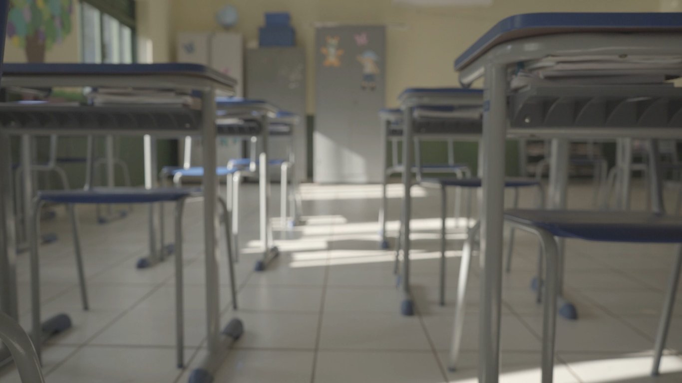 Sala de aula de escola pública, carteiras enfileiradas e lousa; ambiente iluminado e sem pessoas