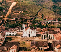 Paisagem urbana com construção histórica em São Roque do Canaã, cercada por vegetação e morros. Crédito: Jacuhy.