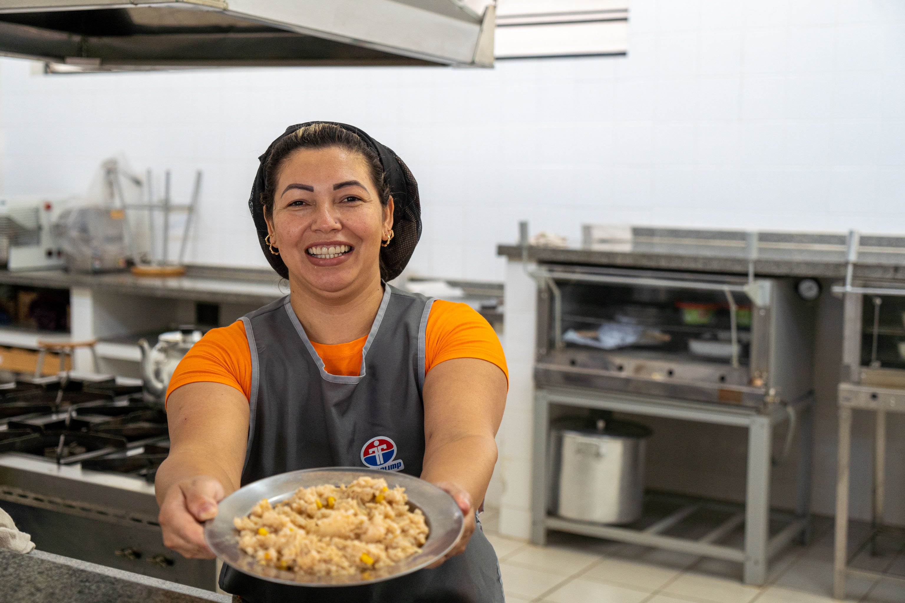 Merendeira em cozinha escolar servindo alimento