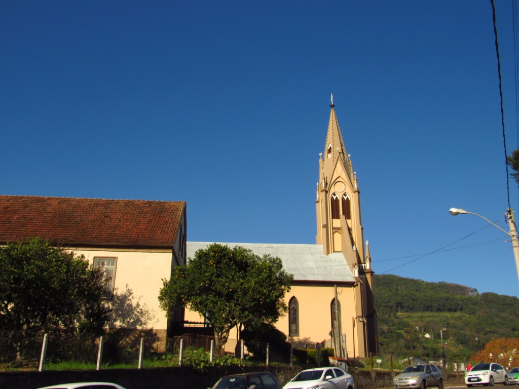 Paisagem urbana serrana no RS, com igreja e morros ao fundo, em fim de tarde