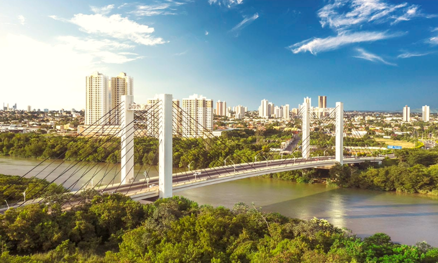 Skyline de Cuiabá ao entardecer, com a ponte sobre o Rio Cuiabá e edifícios iluminados pela luz dourada