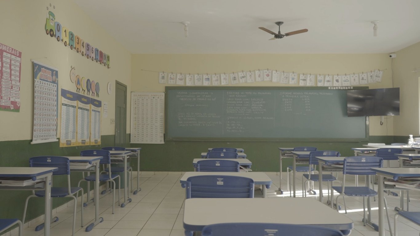 Sala de aula da rede pública no Brasil, com carteiras, quadro e ambiente iluminado