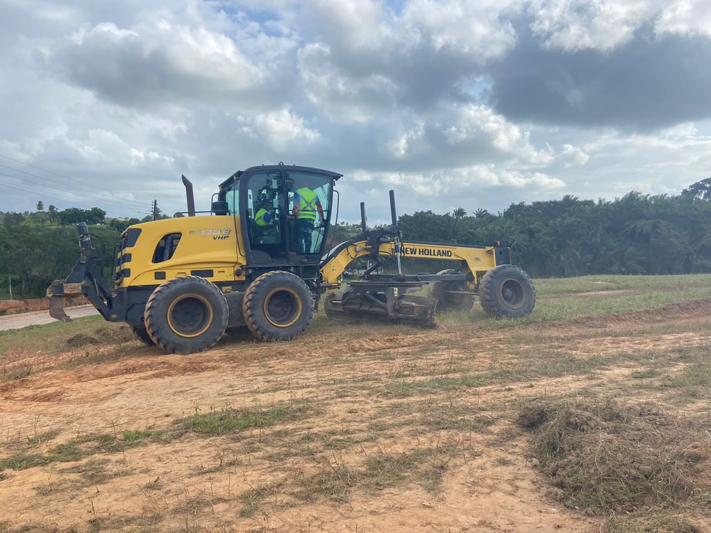 Motoniveladora operando em estrada de terra, com operador usando EPI completo