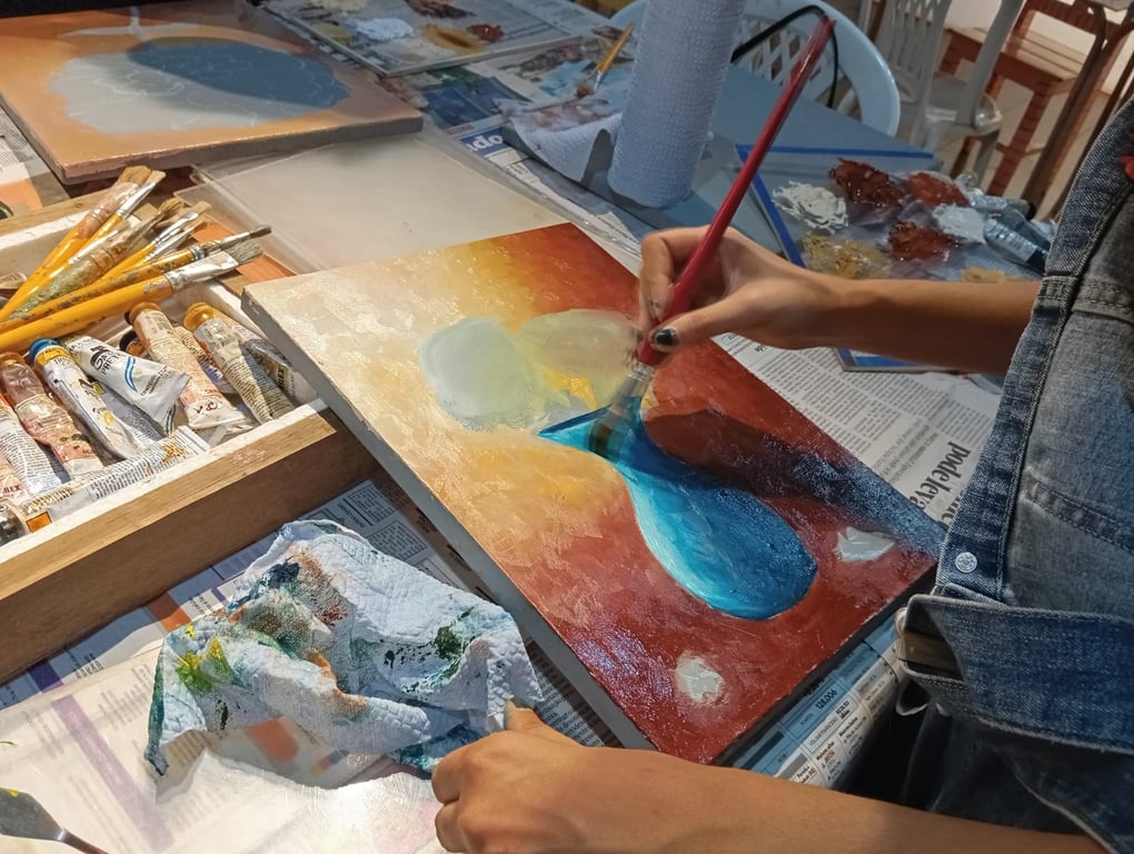 Mesa de aula de artes com pincéis, tintas e telas; ambiente iluminado