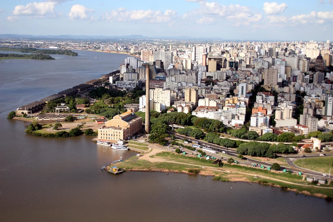 Vista aérea do Centro Histórico de Porto Alegre ao entardecer, com prédios e a orla do Guaíba, em tons dourados e azuis