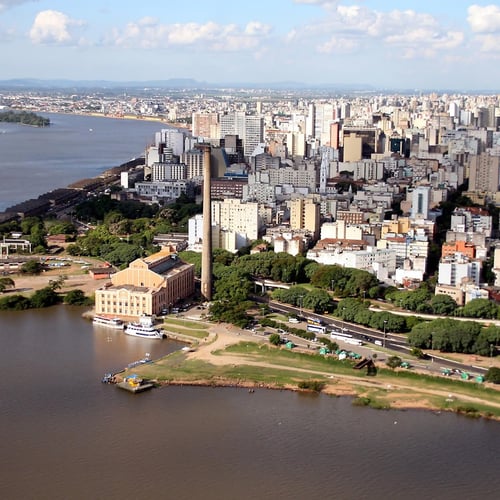 Vista aérea do Centro Histórico de Porto Alegre ao entardecer, com prédios e a orla do Guaíba.