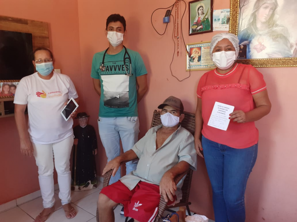 Equipe de enfermagem em visita domiciliar, em ambiente residencial, interagindo com paciente