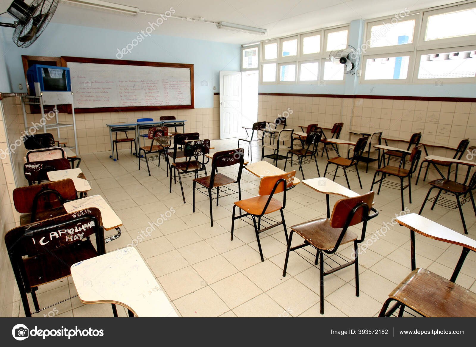 Sala de aula vazia com carteiras e quadro em escola pública