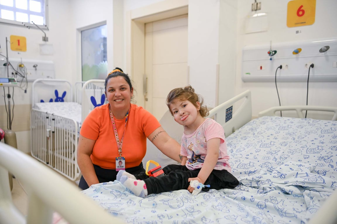 Profissional de saúde atende criança em leito, em ambiente clínico; imagem ilustrativa do atendimento público