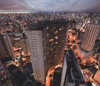 Vista panorâmica de São Paulo ao entardecer, com prédios iluminados e avenida movimentada.