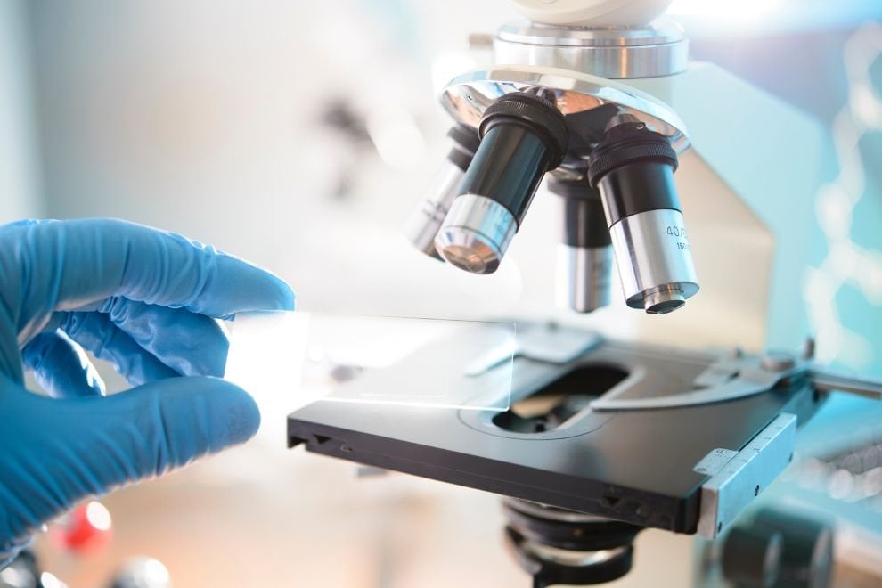 Microscópio com lâmina sendo posicionada, em ambiente de laboratório