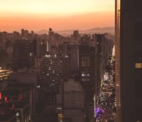 Panorama de São Paulo ao entardecer, com prédios e avenida iluminada.