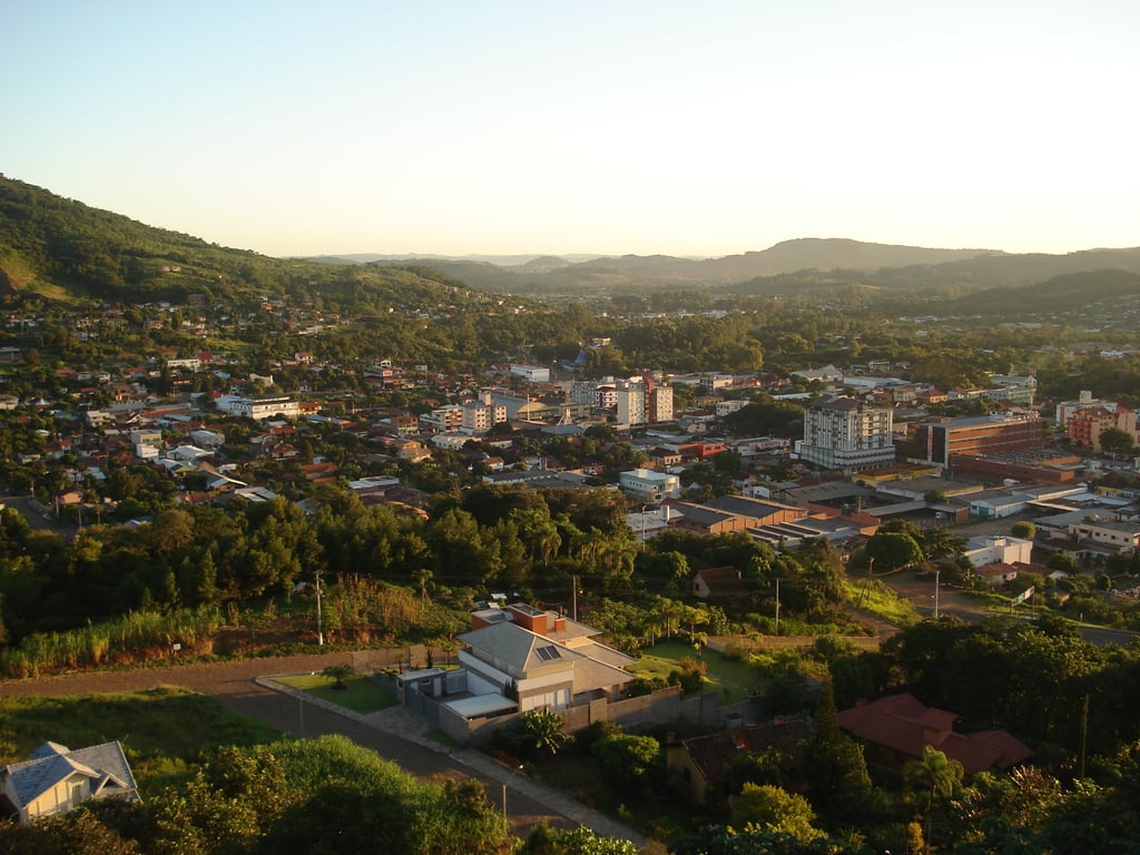 Vista aérea de uma pequena cidade com quarteirões baixos e áreas rurais ao redor. A imagem mostra edificações e vegetação em um ambiente tranquilo.