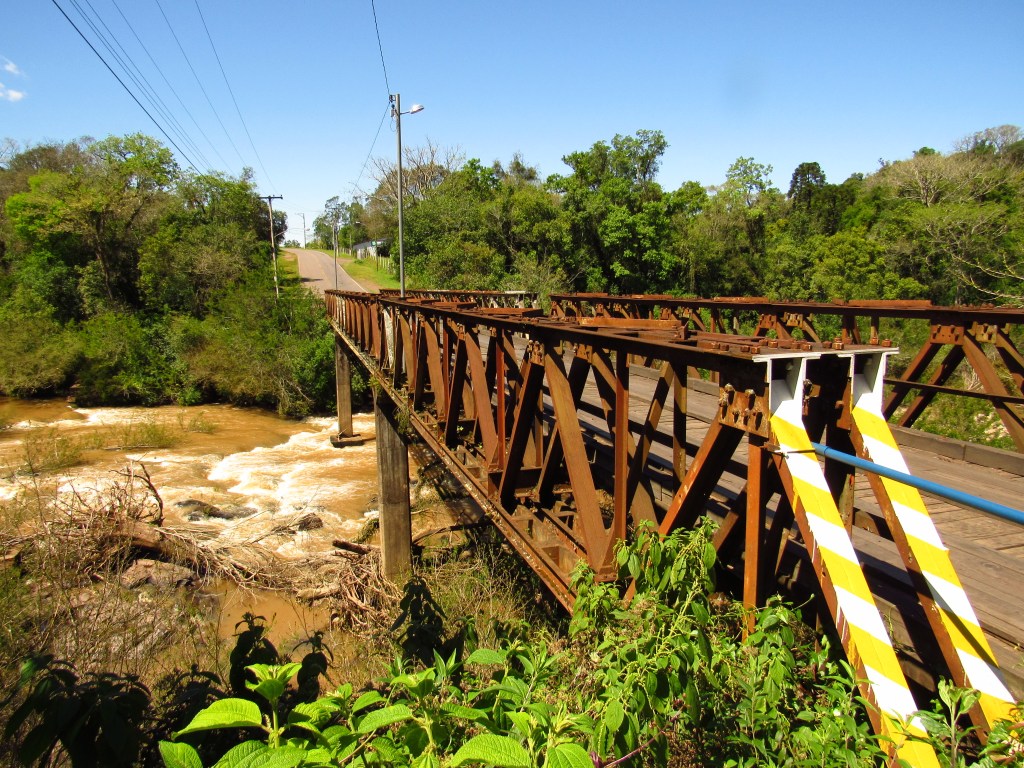 Paisagem do interior do Rio Grande do Sul, com ponte de ferro sobre rio e vegetação nativa