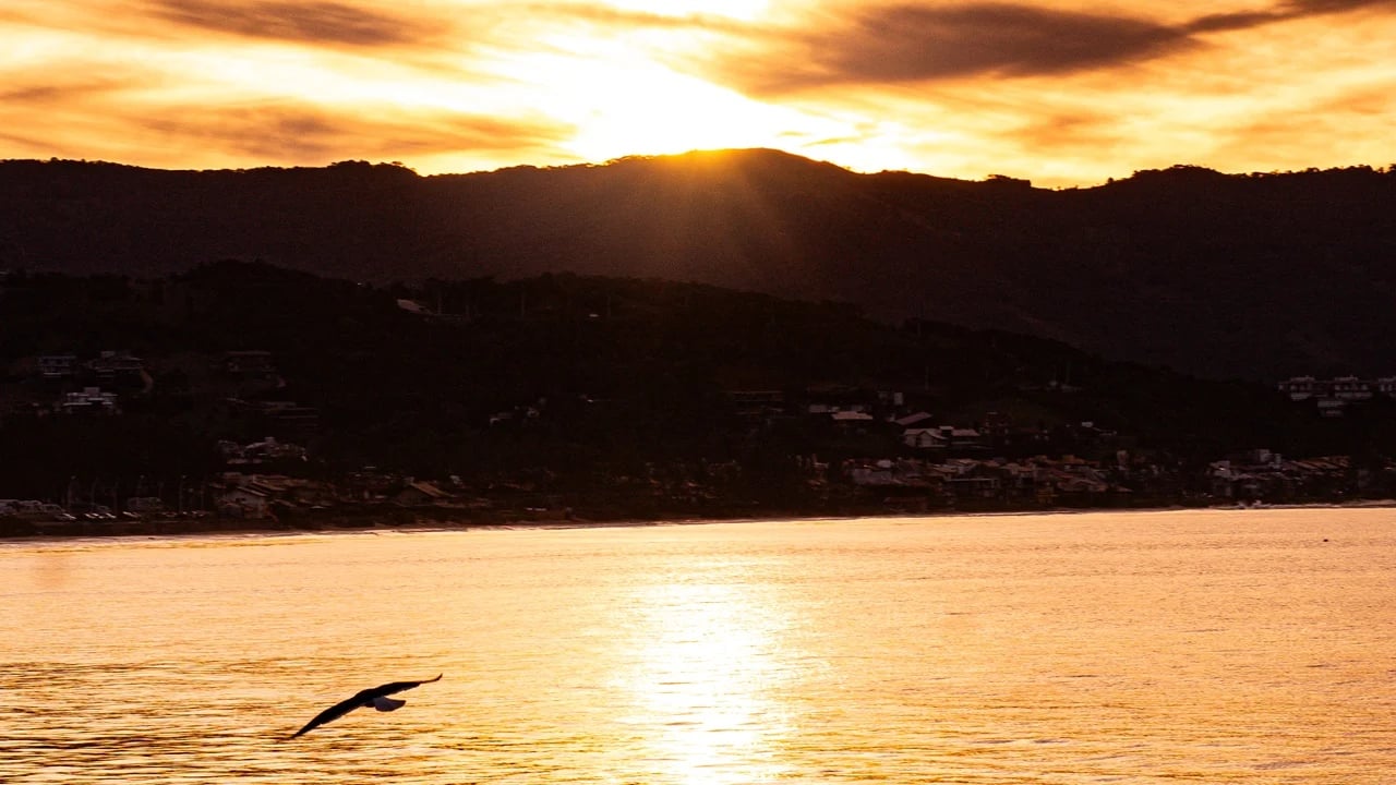 Vista aérea de Garopaba ao entardecer, com mar e morros ao fundo