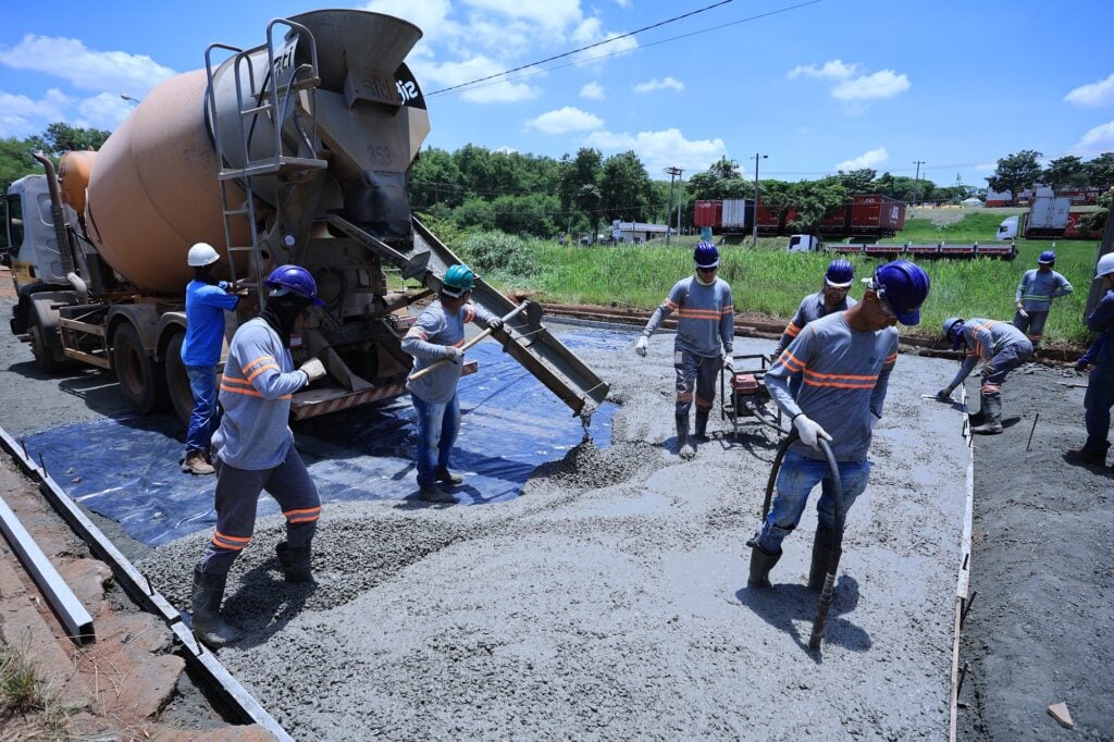Equipe de obras urbanas com maquinário pesado, em via pública, ilustrando funções operacionais municipais