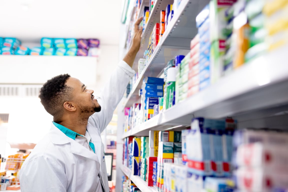 Profissional farmacêutico analisando prateleiras de medicamentos em farmácia moderna
