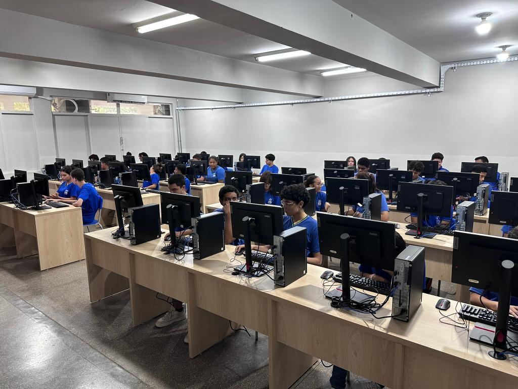 Laboratório de informática com computadores distribuídos em bancadas, em ambiente educacional