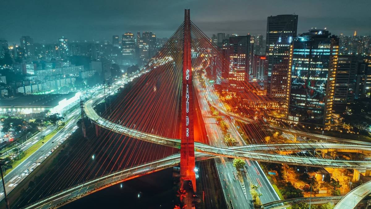 Paisagem urbana noturna de São Paulo, com ponte iluminada, representando a Grande SP