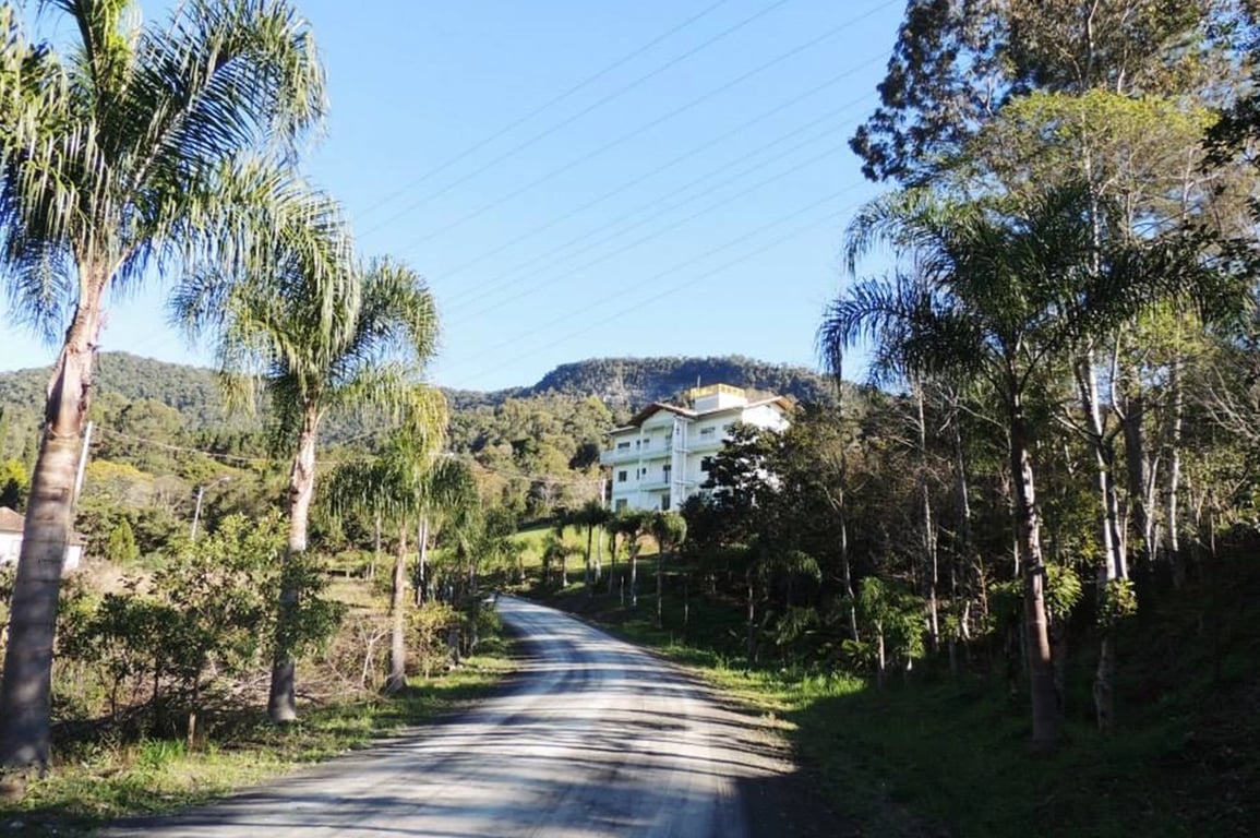 Vista de estrada rural com vegetação e prédios no Alto Vale do Itajaí, em dia ensolarado