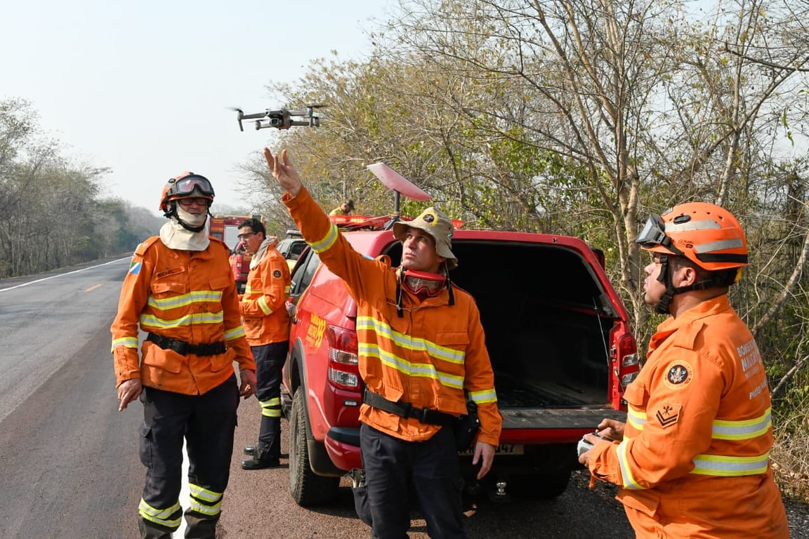 Brigadistas e bombeiros em combate a incêndio florestal, com fumaça ao fundo