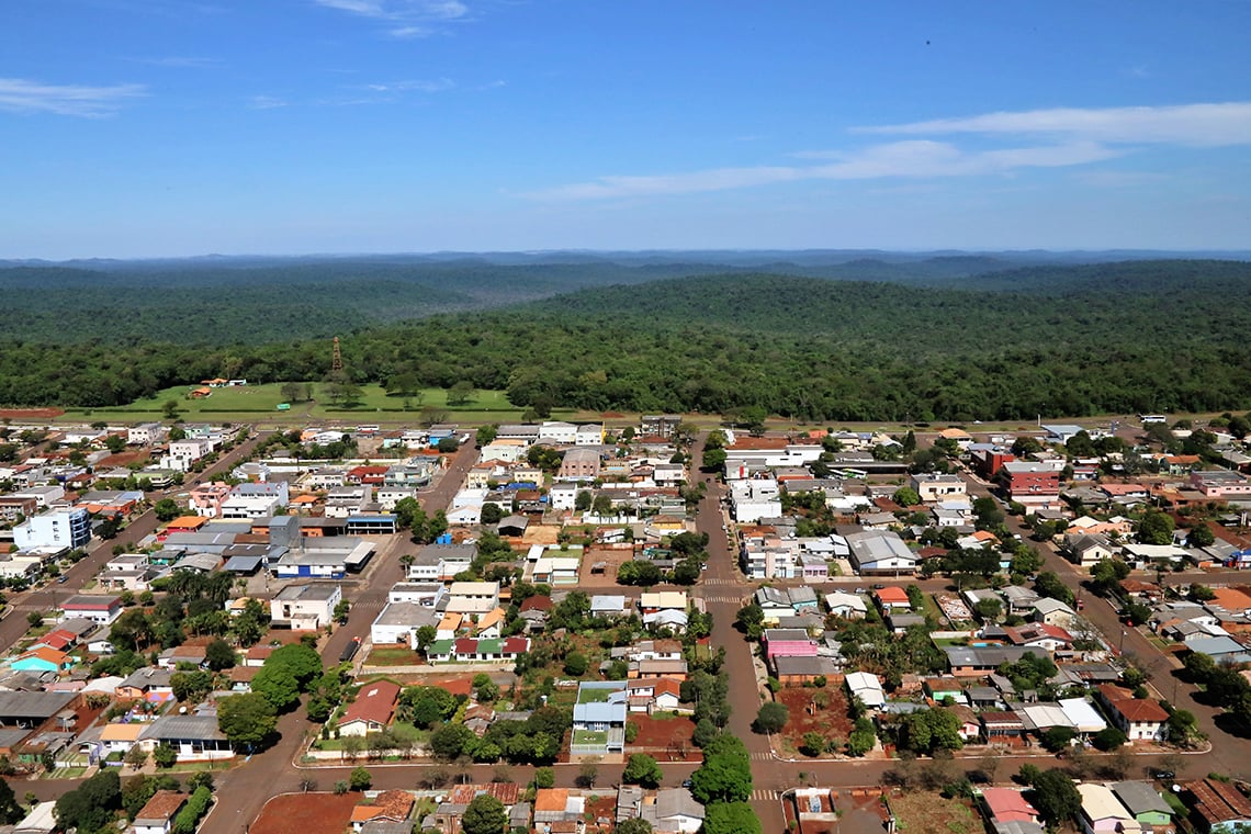 Vista aérea de cidade do interior do Paraná, com áreas verdes e céu azul