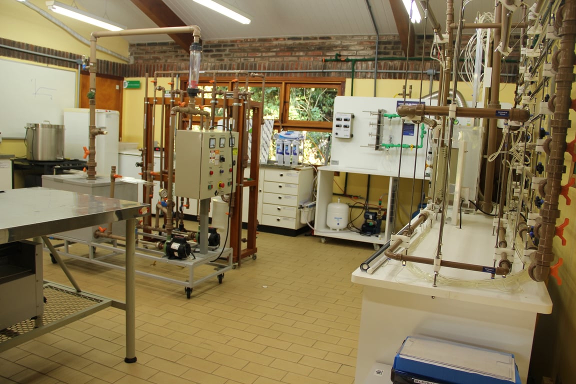 Laboratório escolar de Química com bancadas, vidrarias e equipamentos; ambiente iluminado e organizado.