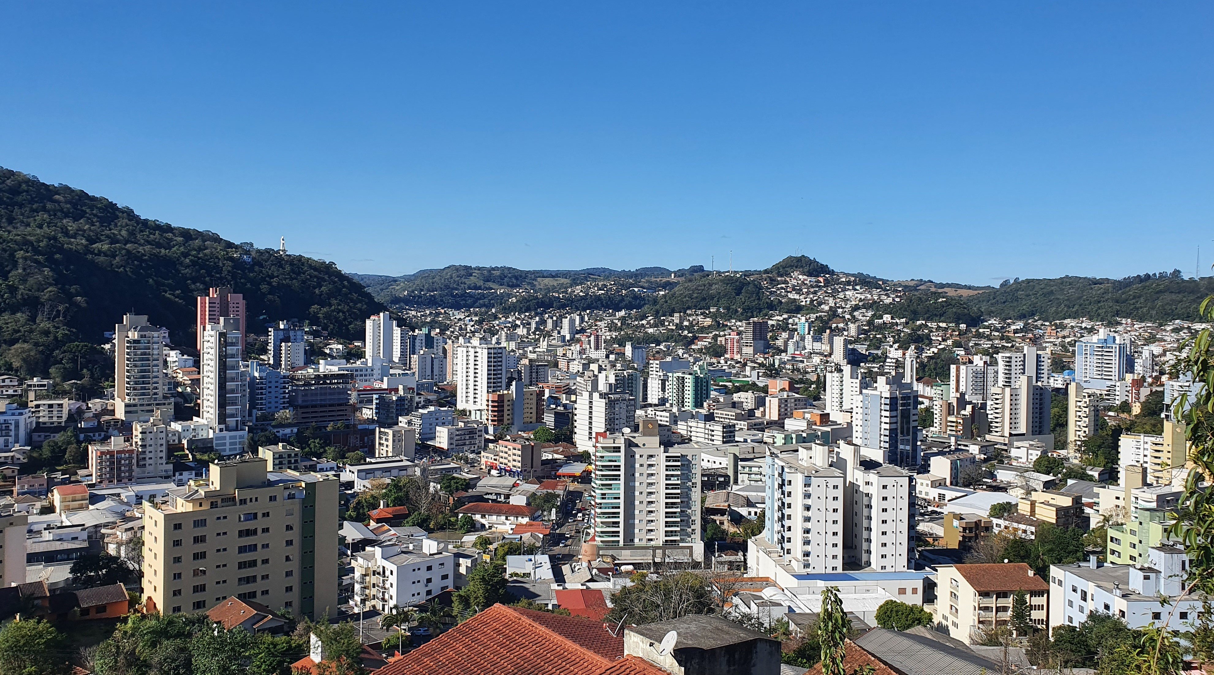 Vista de Joaçaba SC, com prédios e colinas ao fundo, em dia ensolarado