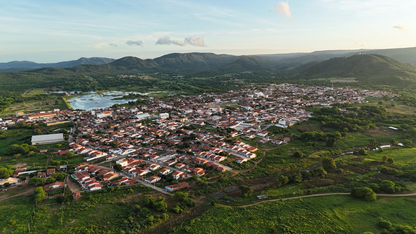 Vista aérea de pequena cidade do interior com vegetação e serras ao fundo