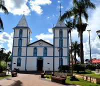 Praça arborizada com igreja histórica em cidade do interior de Goiás, sob céu azul