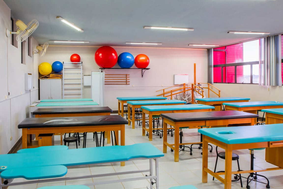Laboratório acadêmico de fisioterapia musculoesquelética com mesas de avaliação e equipamentos, em ambiente universitário, composição horizontal.
