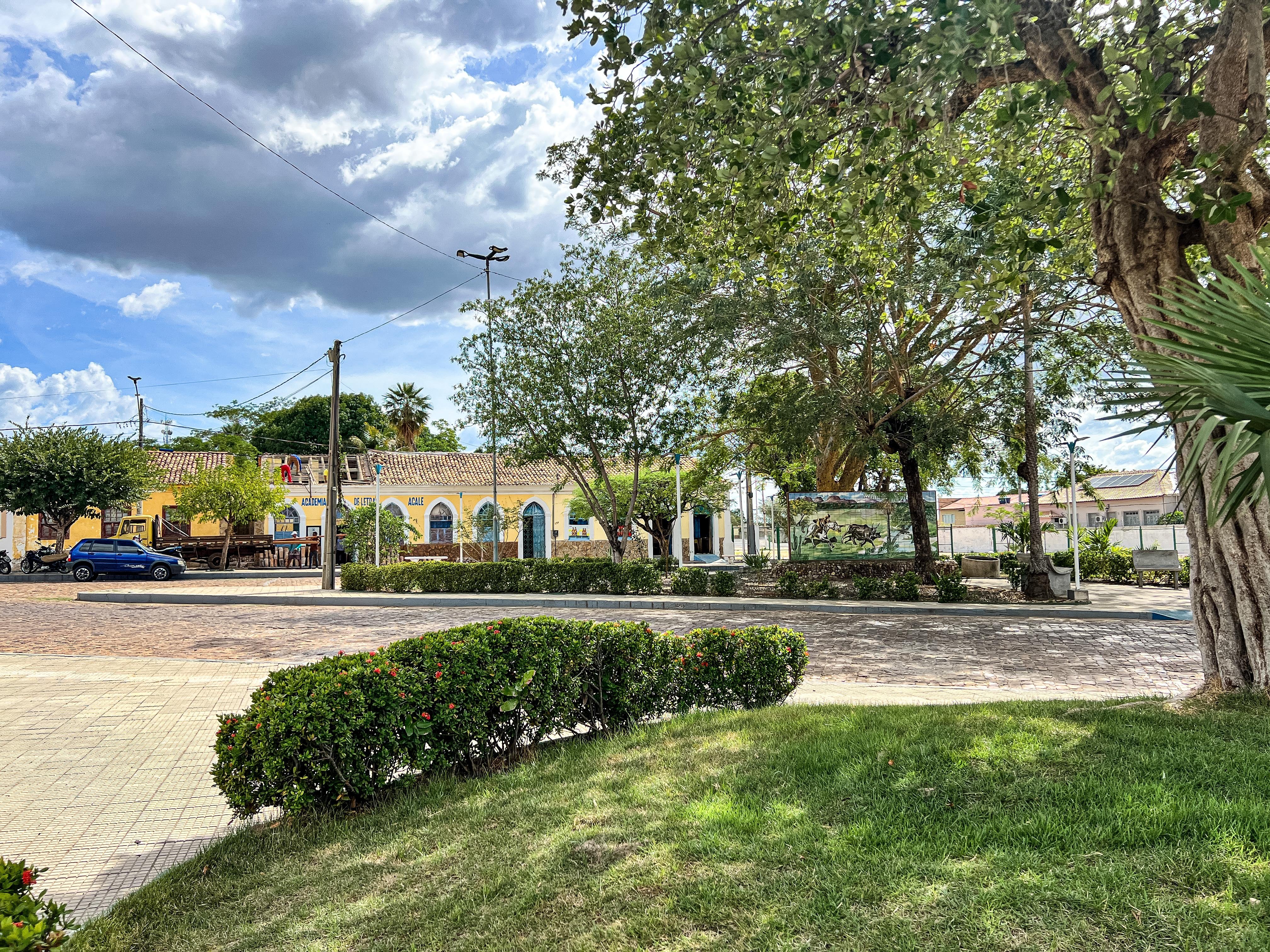 Praça central no interior do Piauí, com prédios baixos e vegetação, em dia ensolarado