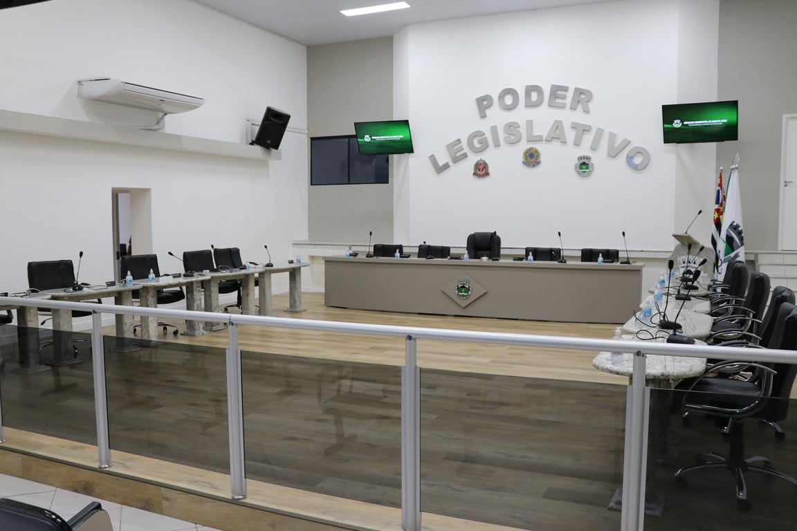 Interior de uma câmara municipal vazia, com bancadas e cadeiras organizadas