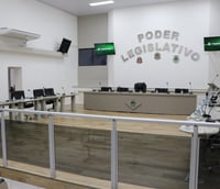 Interior de uma câmara municipal vazia, com bancadas e cadeiras organizadas.